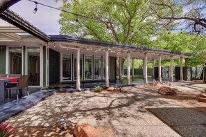 A covered patio area with a dining setup, a pergola with string lights, and a landscaped garden with rocks and a small plant.