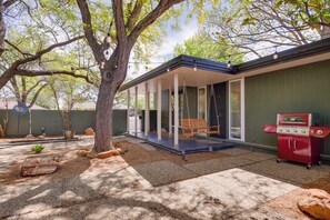 A covered patio with a swing, a barbecue grill, and a tree providing shade.