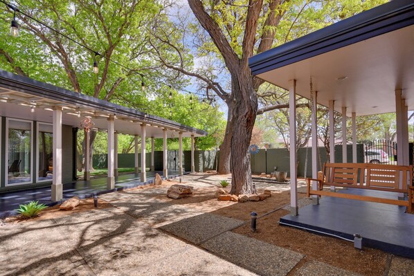 A covered outdoor area with a wooden bench, stone pathway, and a pergola with string lights.