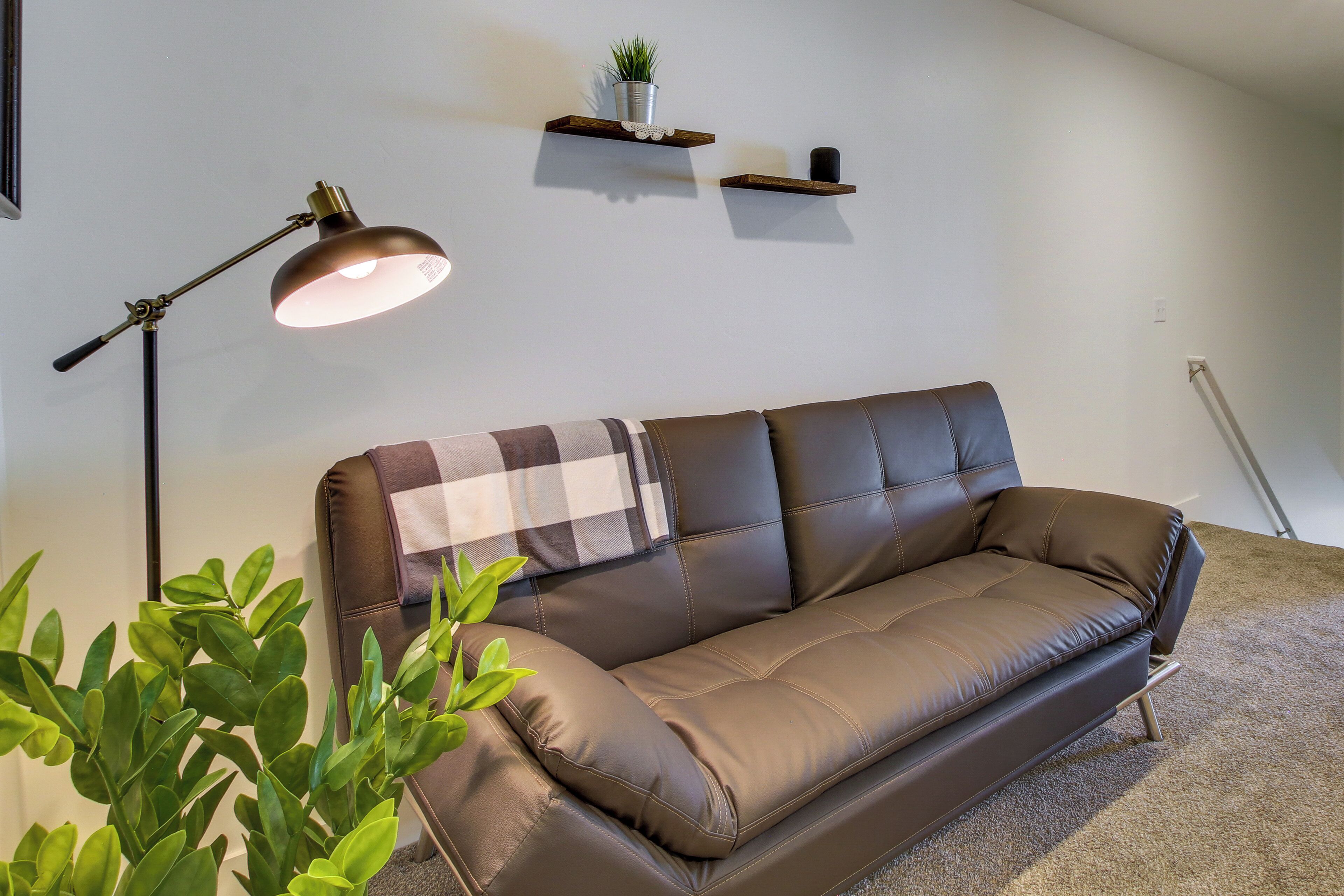 A brown leather sofa with a plaid throw blanket, a floor lamp, and a potted plant.