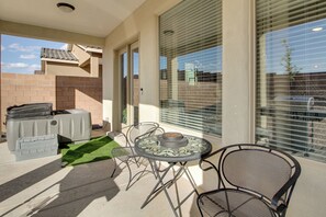 A patio with a round table and chairs, a barbecue grill, and a small rug.