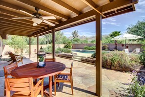 An outdoor patio with a wooden table and chairs, a ceiling fan, and a view of a swimming pool and desert landscape. - Stylish Tucson Home w/ Patio & Private Pool! (Tucson)