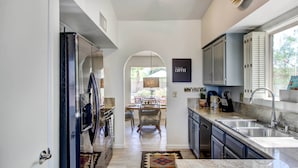 A modern kitchen with a central island, stainless steel appliances, and a view to the outdoor dining area. - Stylish Tucson Home w/ Patio & Private Pool! (Tucson)