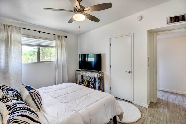 A bedroom with a bed, a ceiling fan, a television on a stand, and a door. - Stylish Tucson Home w/ Patio & Private Pool! (Tucson)