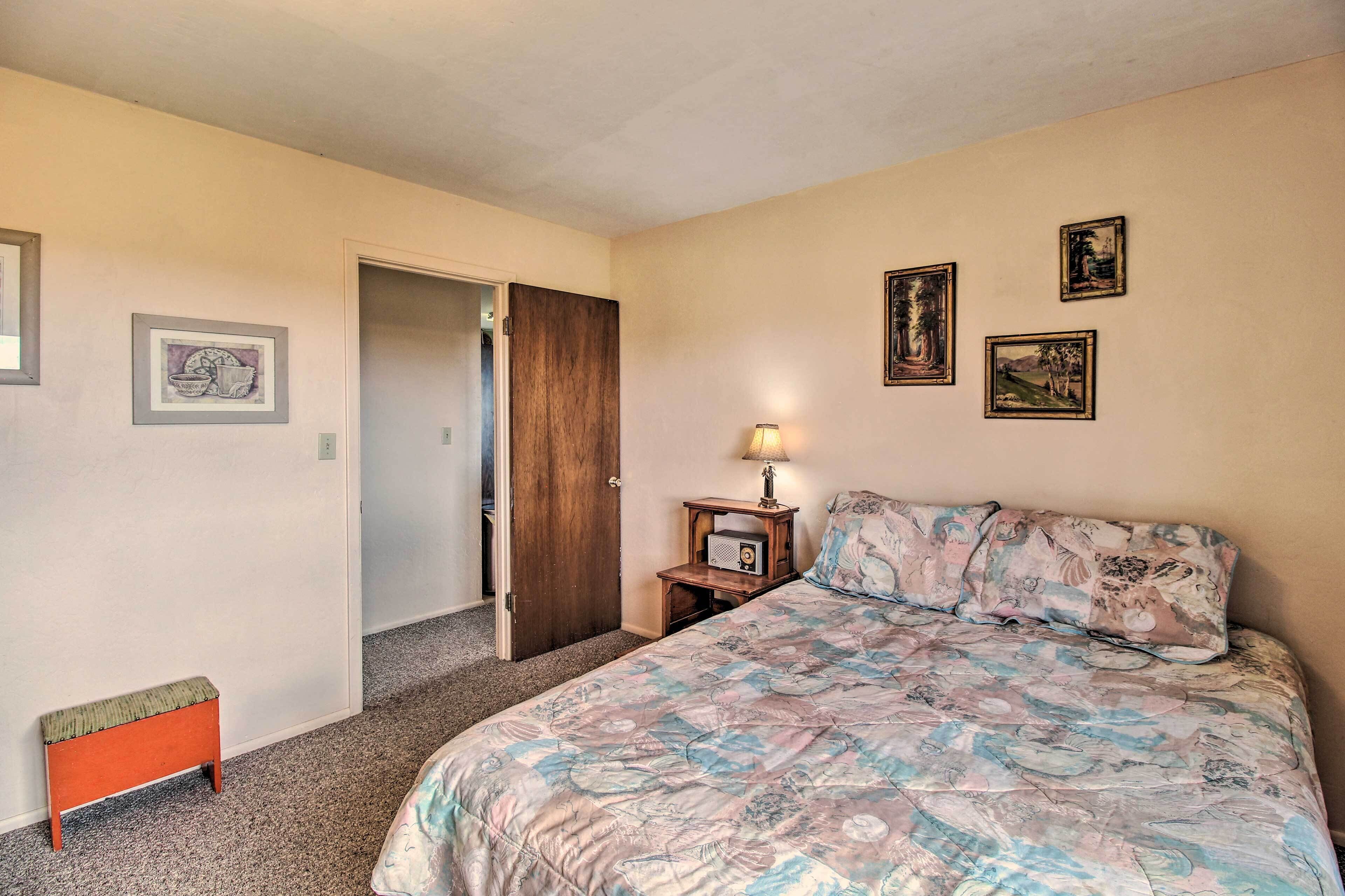 A bedroom with a bed, a nightstand with a lamp, a door, and three framed pictures on the wall.