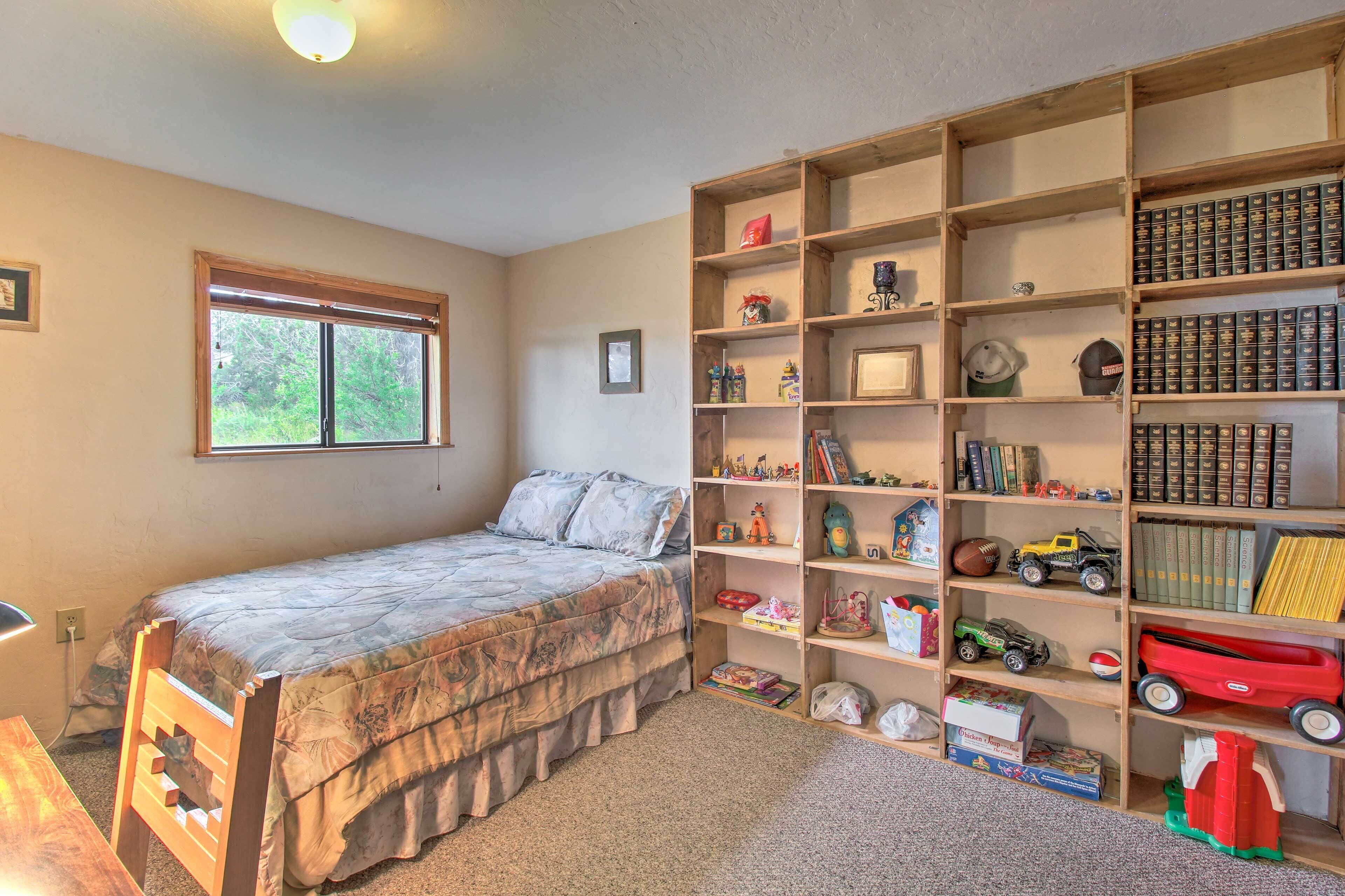 A bedroom with a bed, a window, a bookshelf, and a desk.