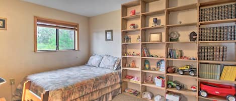 A bedroom with a bed, a window, a bookshelf, and a desk.