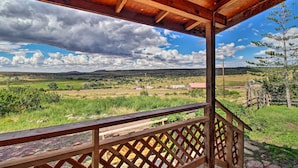 A wooden deck with a view of a rural landscape, including fields, a few buildings, and distant hills.
