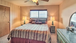 A bedroom with a large bed, a ceiling fan, a window with a view, two bedside tables with lamps, and a dresser with a mirror.