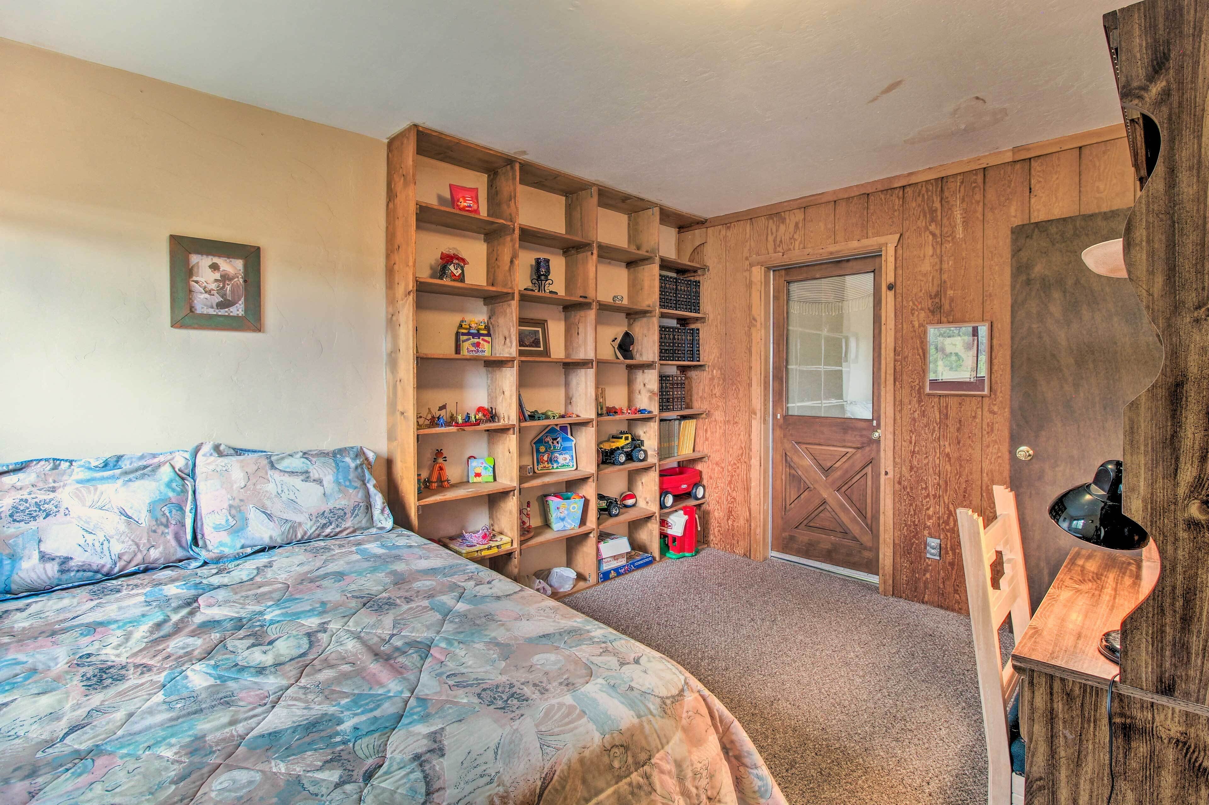 A bedroom with a bed, wooden shelves filled with toys, and a door.
