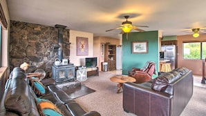 A cozy living room with a stone fireplace, leather sofas, a fan, and a ceiling fan.
