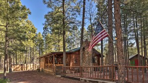 A rustic cabin with a porch, surrounded by tall pine trees and a clear sky. - Family & Dog Friendly: Rustic Lakeside Cabin (Lakeside)