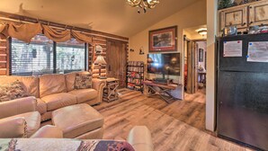 A cozy living room with a leather sofa, a bookshelf, and a dining area with a table and chairs. - Family & Dog Friendly: Rustic Lakeside Cabin (Lakeside)