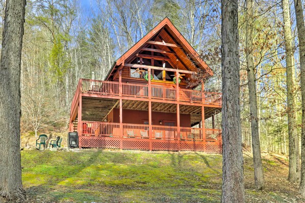 A two-story cabin with a balcony, surrounded by trees.