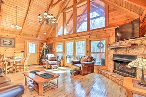 A spacious log cabin interior with a fireplace, wooden furniture, and large windows.