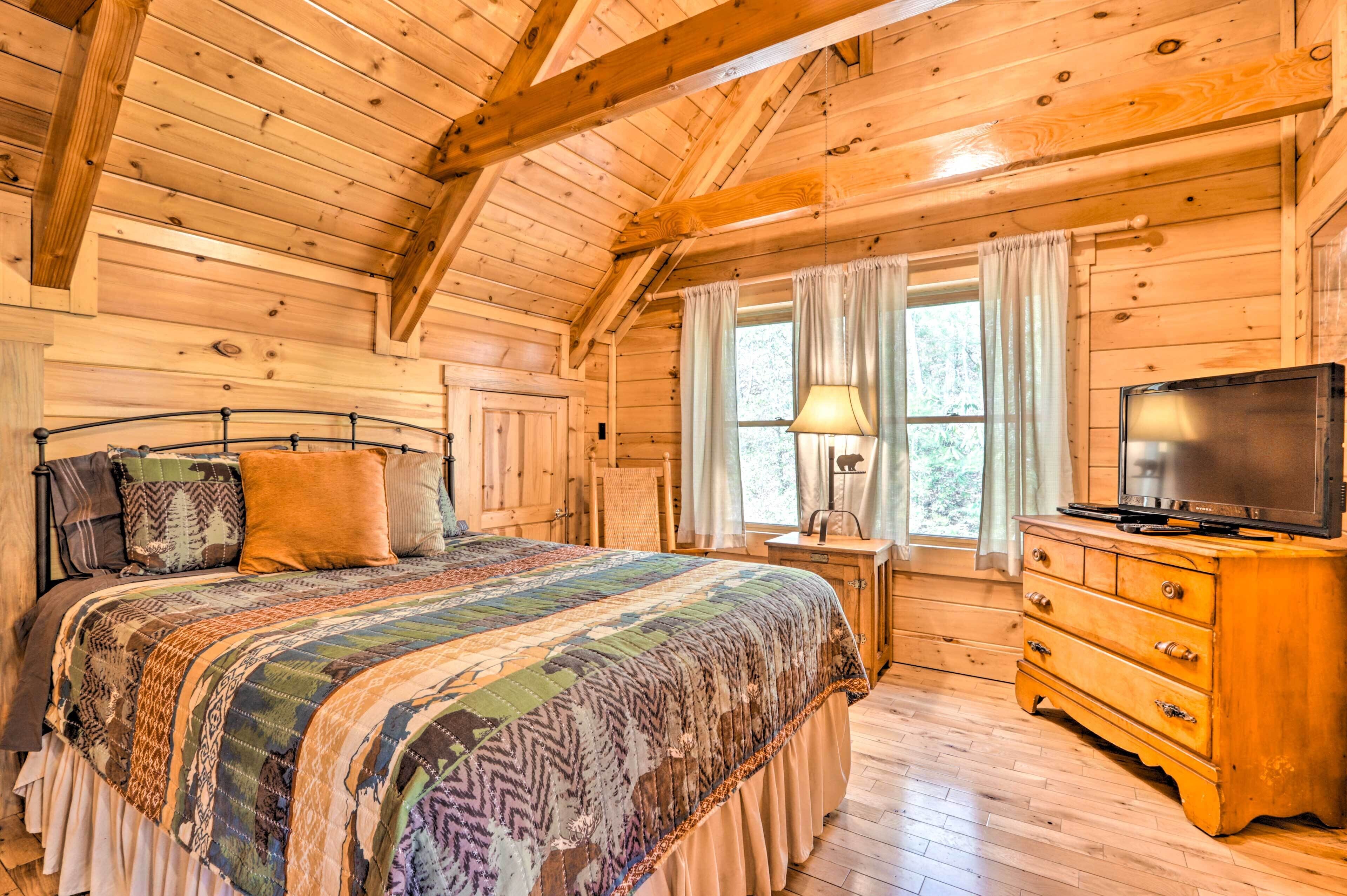 A wooden cabin bedroom with a large bed, a wooden dresser, and a television.