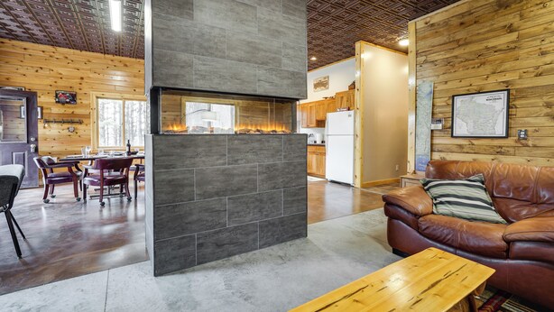 Ein modernes Interieur mit Kamin aus Stein, Holzwänden, einer Ledersofa und einem Essbereich.
