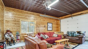 Ein Blockhaus-Interieur mit Holzbalkendecke, einem roten Sofa, einem braunen Ledersessel und einer sitzenden Person.