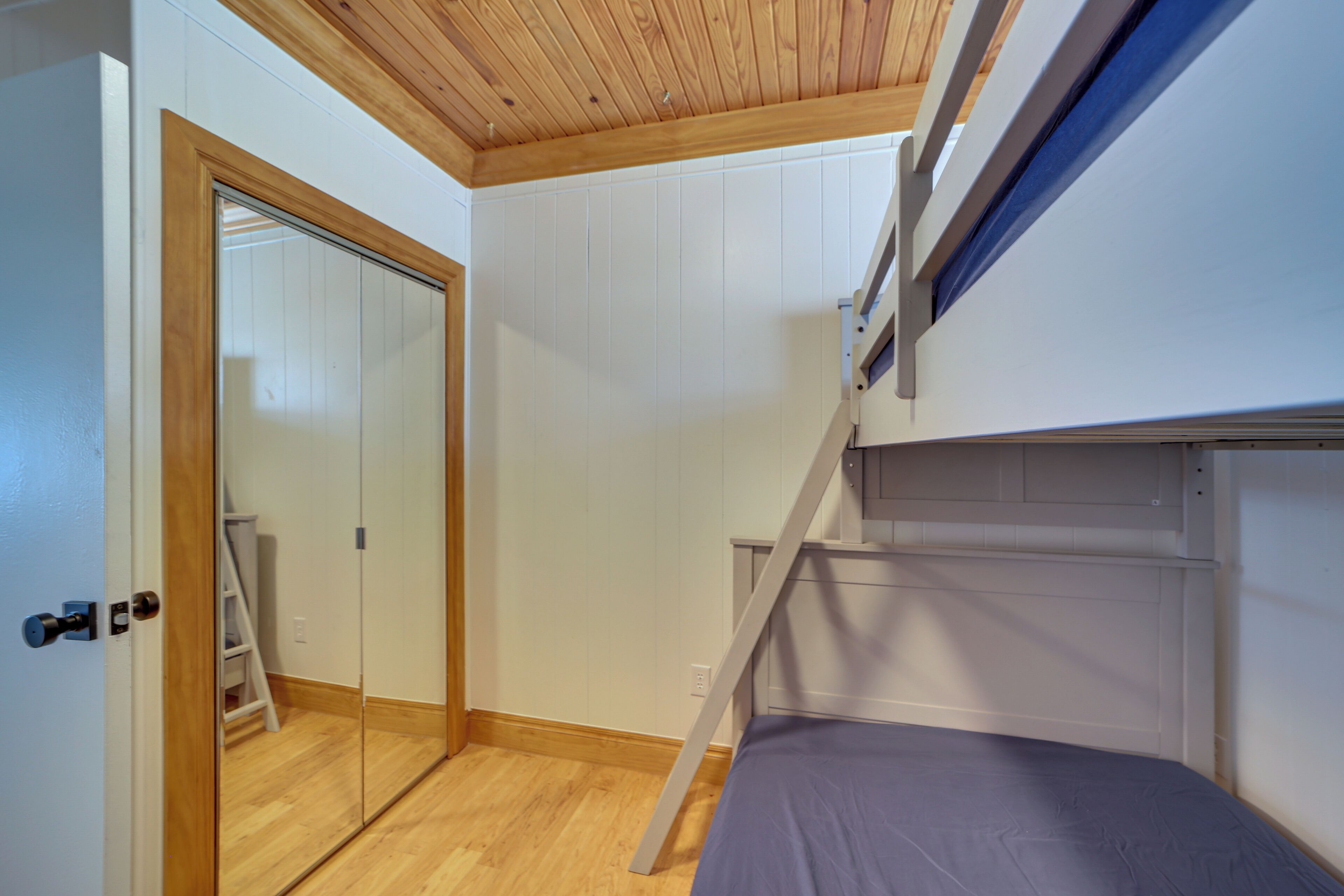 A room with a bunk bed, wooden flooring, a white door, and a mirror on the wall.