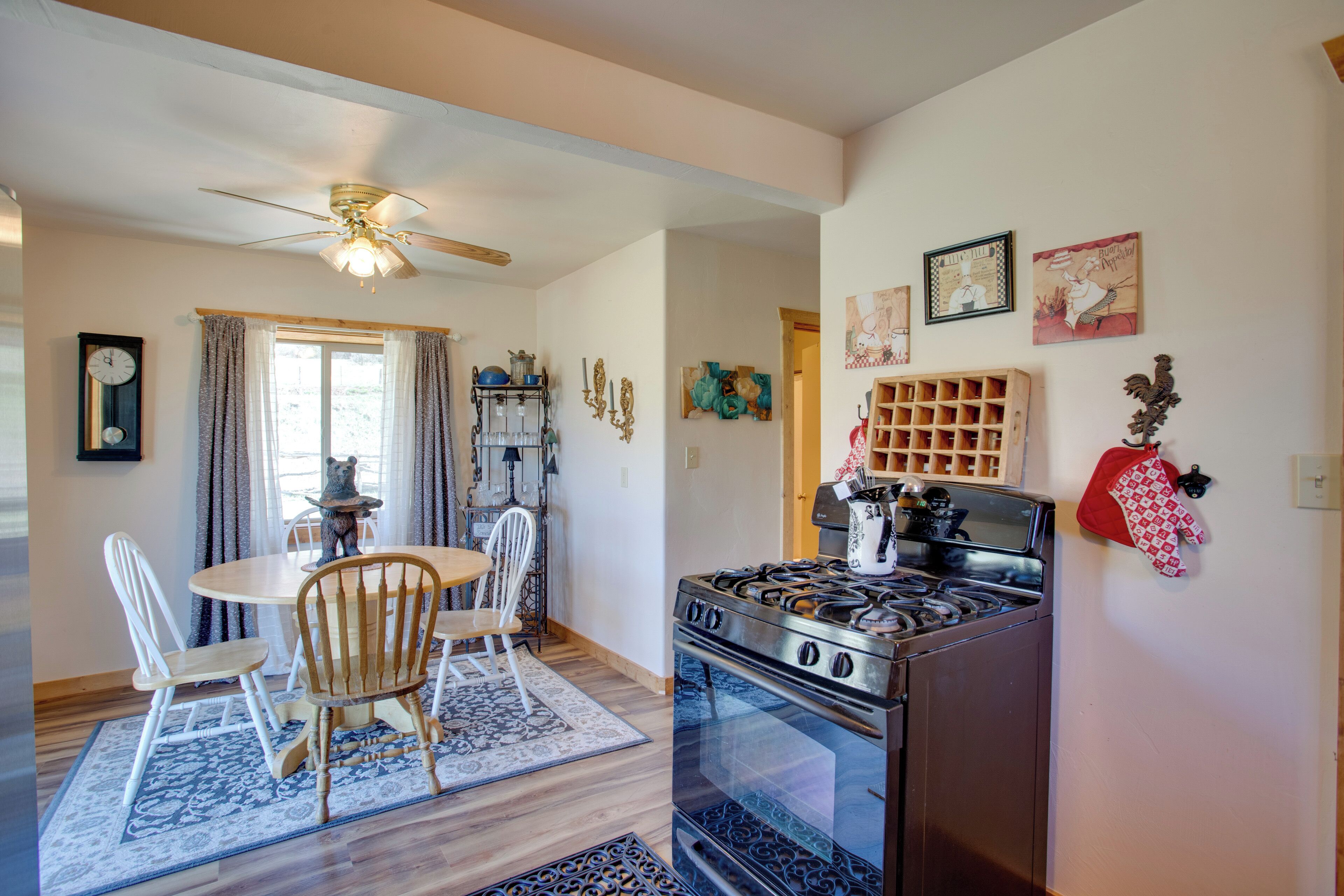 A kitchen with a stove, chairs, a dining table, and a ceiling fan.