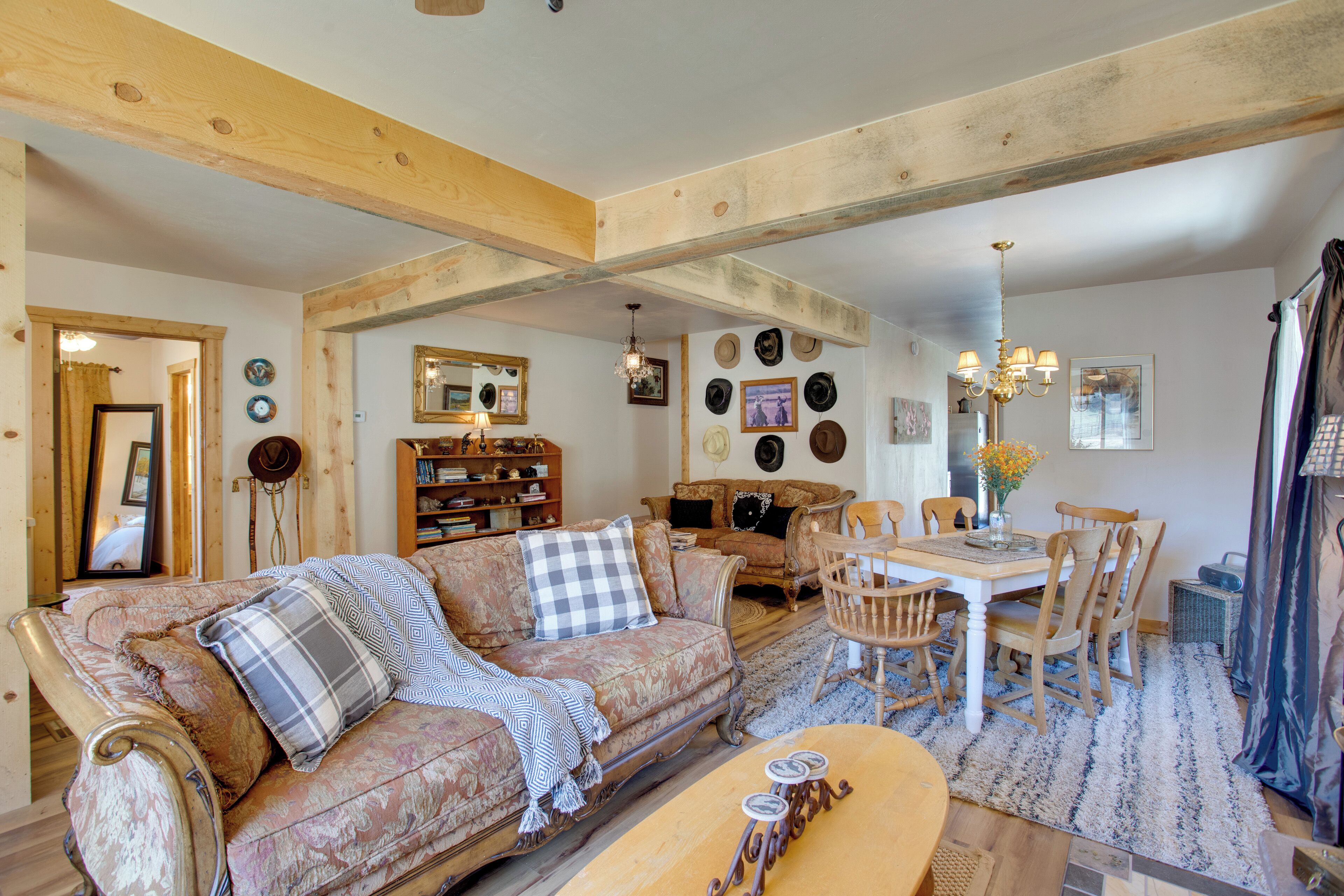 A cozy living room with a sofa, dining table, and chairs. There are hats and a mirror on the wall.