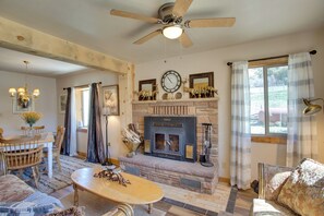 A cozy living room with a fireplace, a dining area, and a ceiling fan.