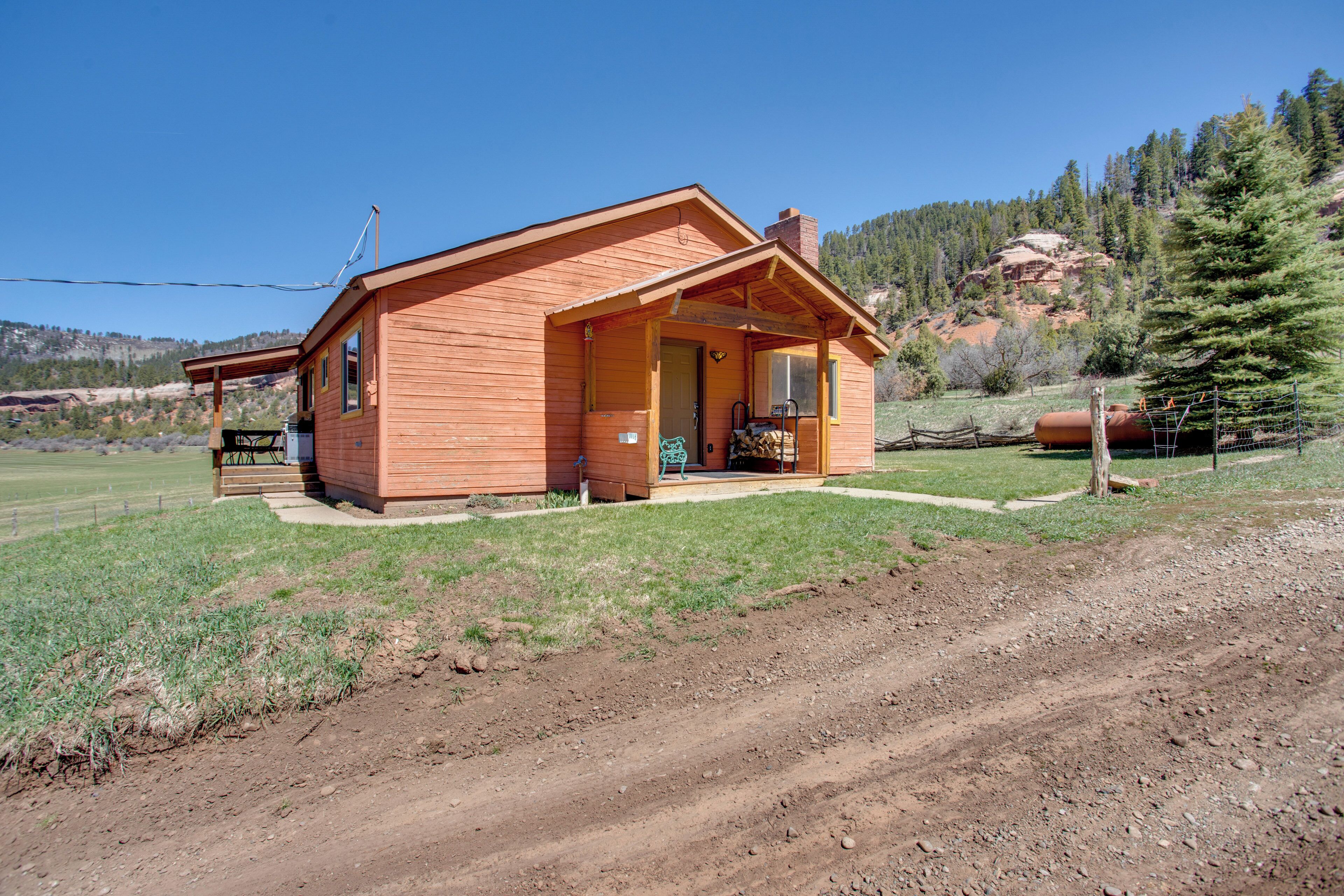 A wooden cabin with a porch, a small outdoor seating area, and a dirt path leading to it. - Cozy Dolores Getaway: Hike, Fish + More! (Dolores)