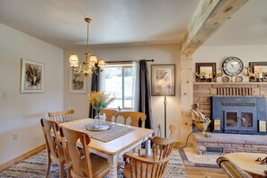 A dining area with a wooden table and chairs, a chandelier, and a fireplace with decorative items.