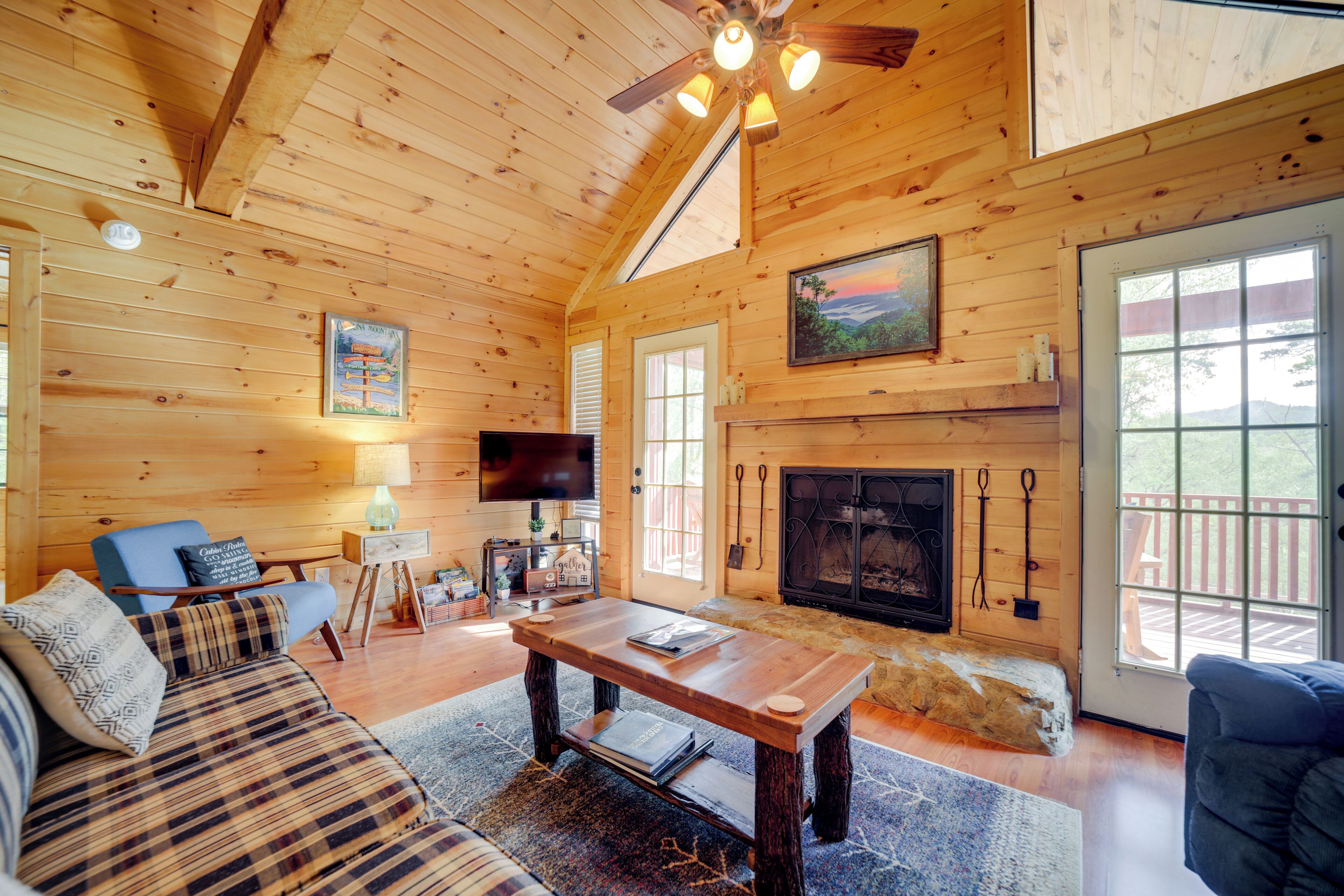 A cozy cabin interior with a wooden ceiling, a fireplace, a television, and a sofa.