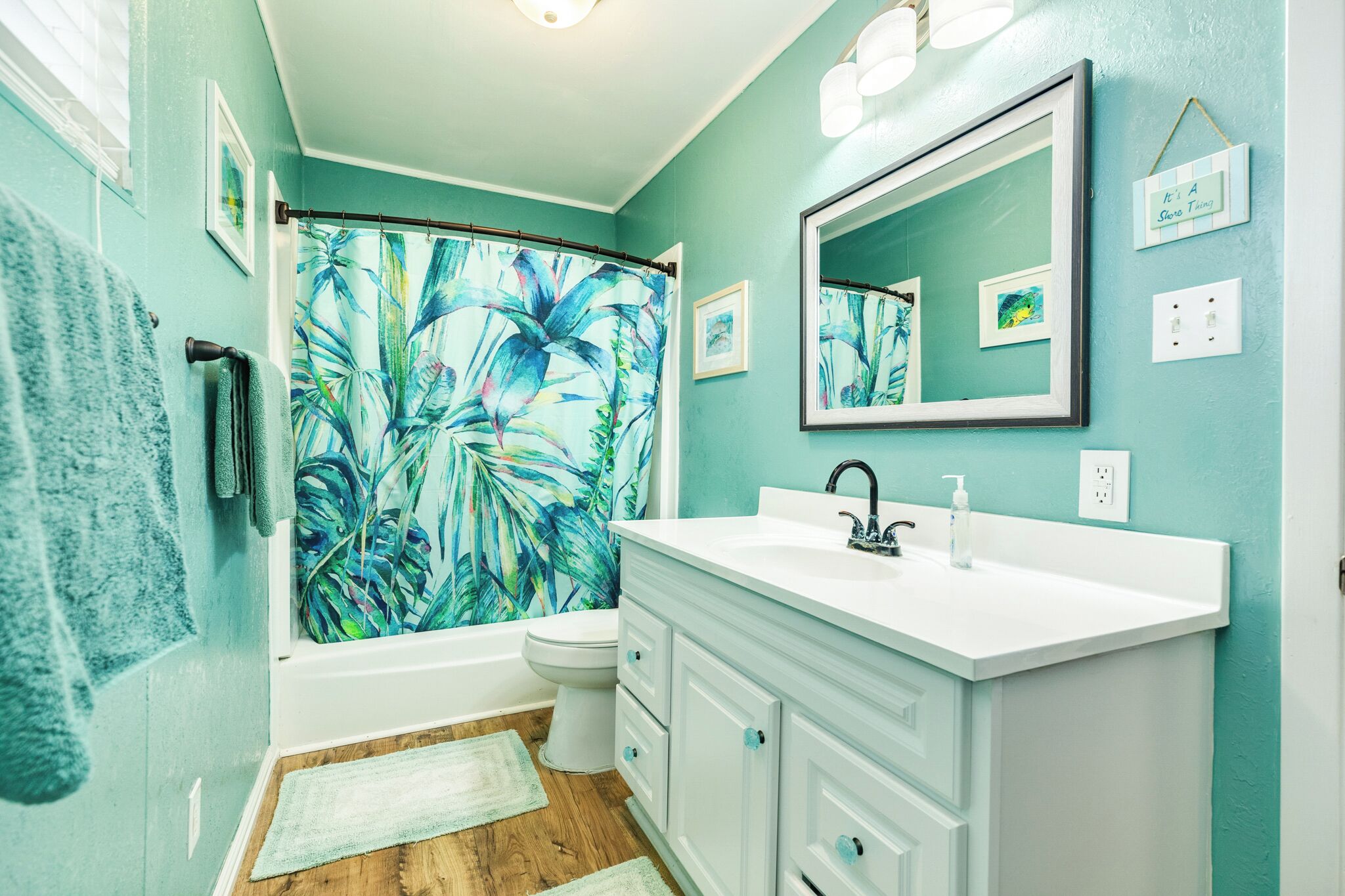 A bathroom with a bathtub, a toilet, a sink, and a shower curtain with a tropical leaf pattern.