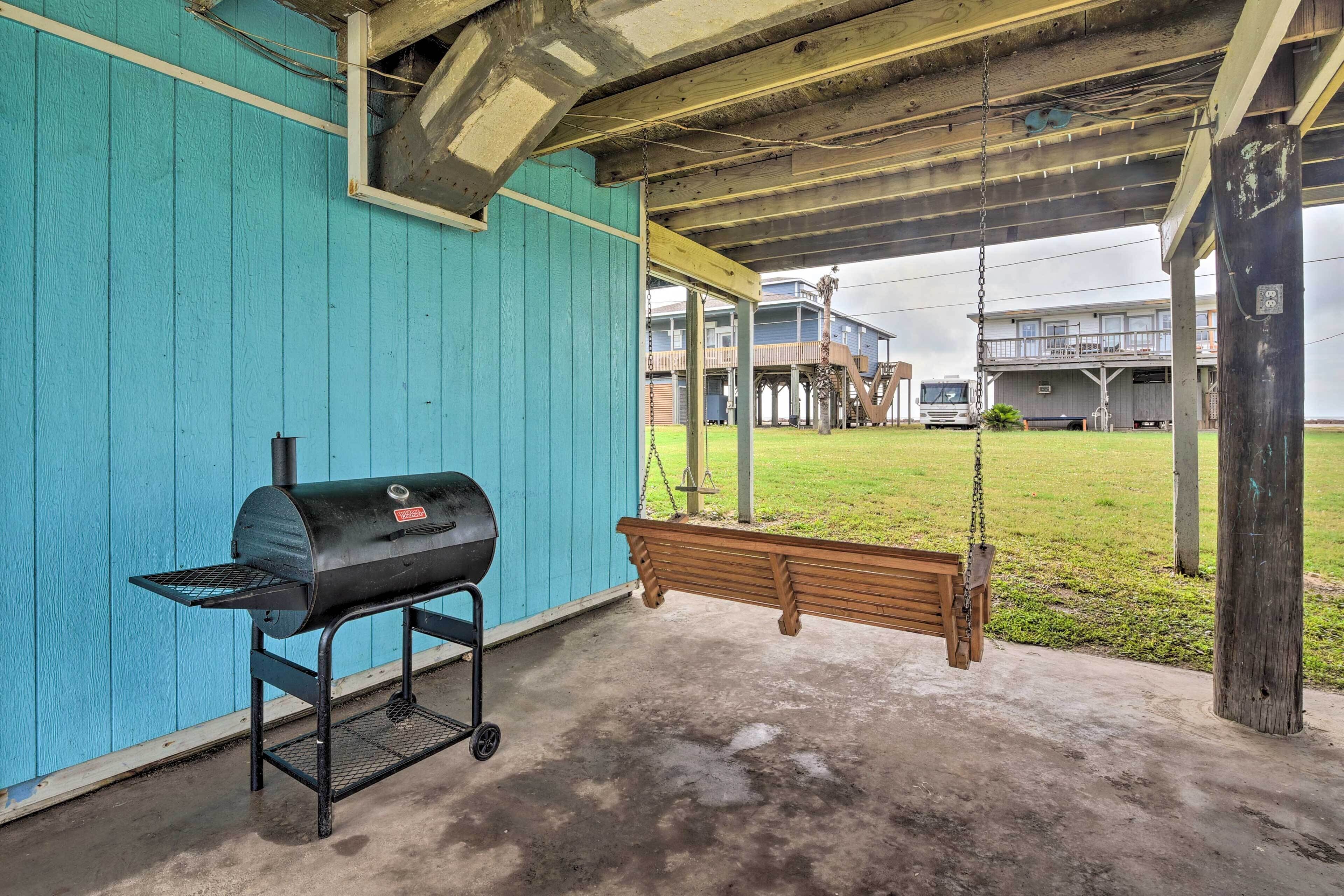 Ein überdachter Außenbereich mit Grill, Schaukel und Blick auf ein Gebäude im Hintergrund.