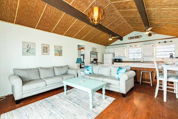 Un soggiorno con un divano azzurrognolo, un tavolino da caffè coordinato e un angolo cottura con mobili bianchi e un soffitto in legno.