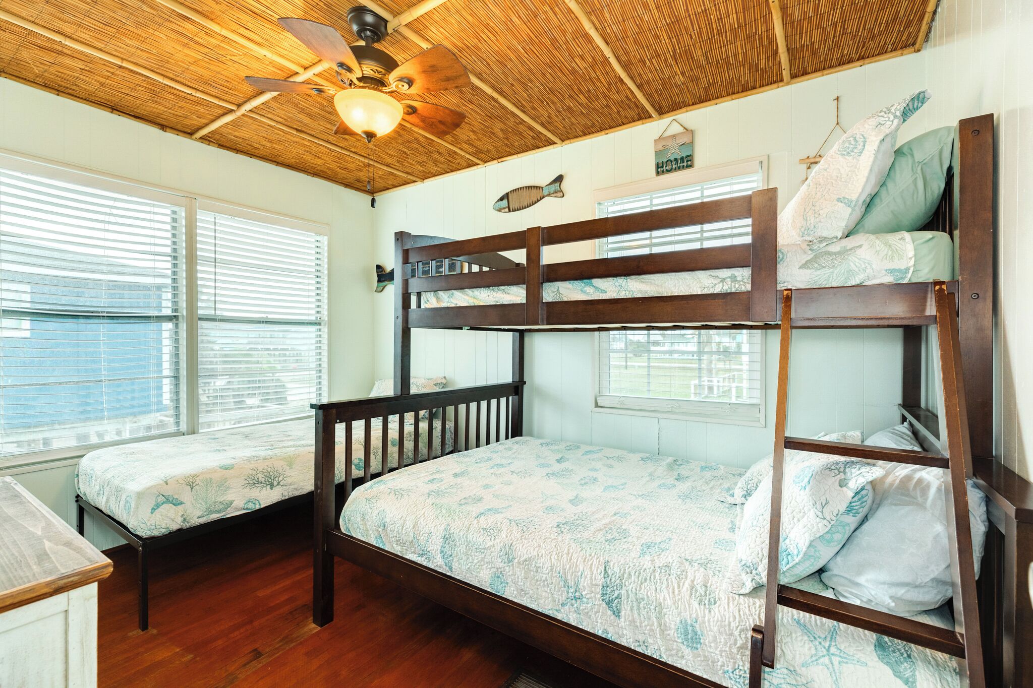 Quarto com duas camas beliche, ventilador de teto e janela com persianas.