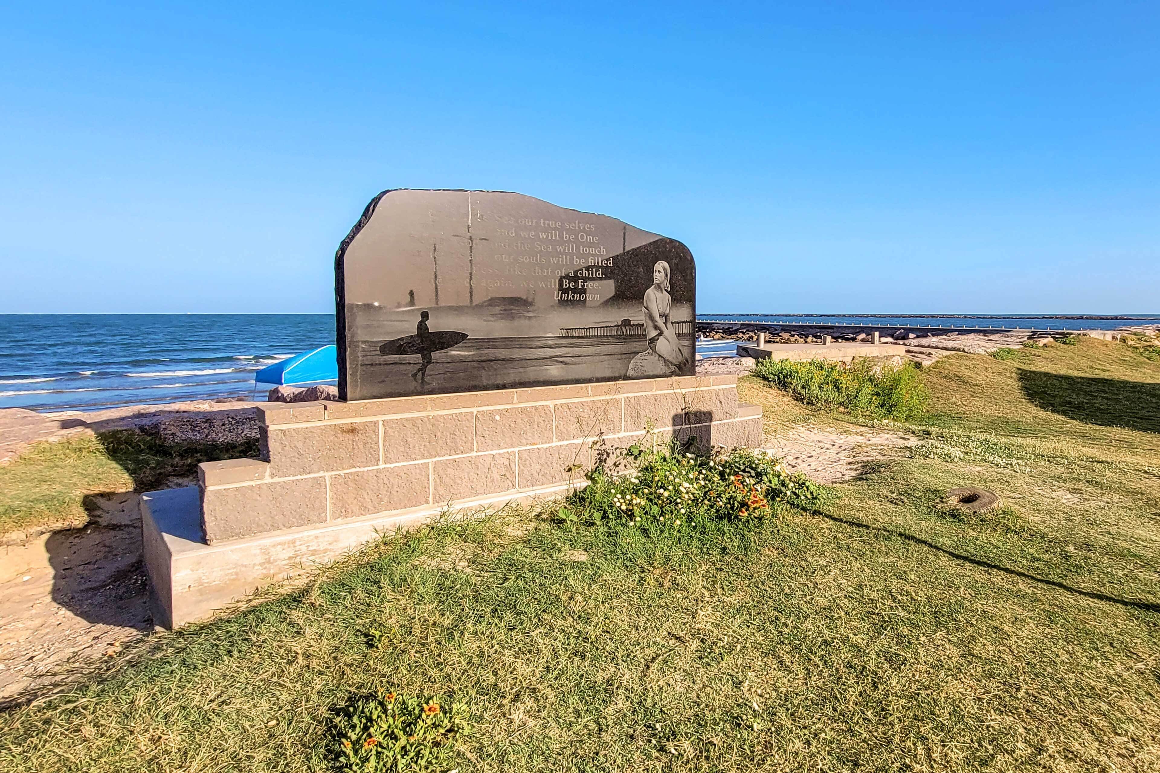 A beachside memorial with a mural and a surfboard.