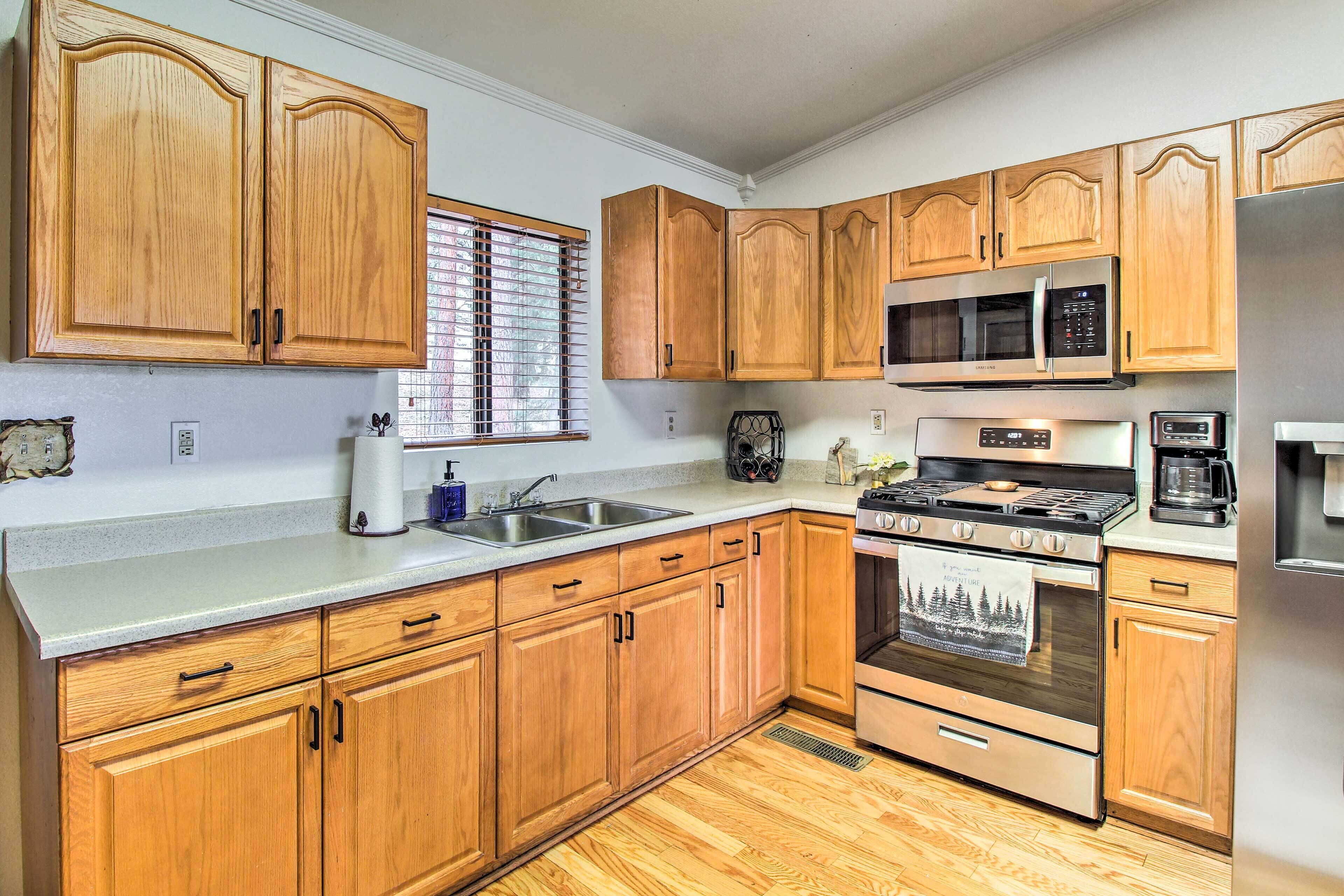 A kitchen with wooden cabinets, a stainless steel sink, a microwave, a stove, and a refrigerator.