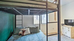 A bunk bed with a metal frame, a green wall, a window with a view of trees, a dresser with a TV, and a moose plush toy on the bed. - Peaceful Nutrioso Cabin Retreat w/ Mountain Views! (Eagar)