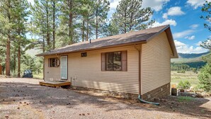 A small, single-story cabin with a front porch, surrounded by a gravel driveway and a forested landscape. - Peaceful Nutrioso Cabin Retreat w/ Mountain Views! (Eagar)