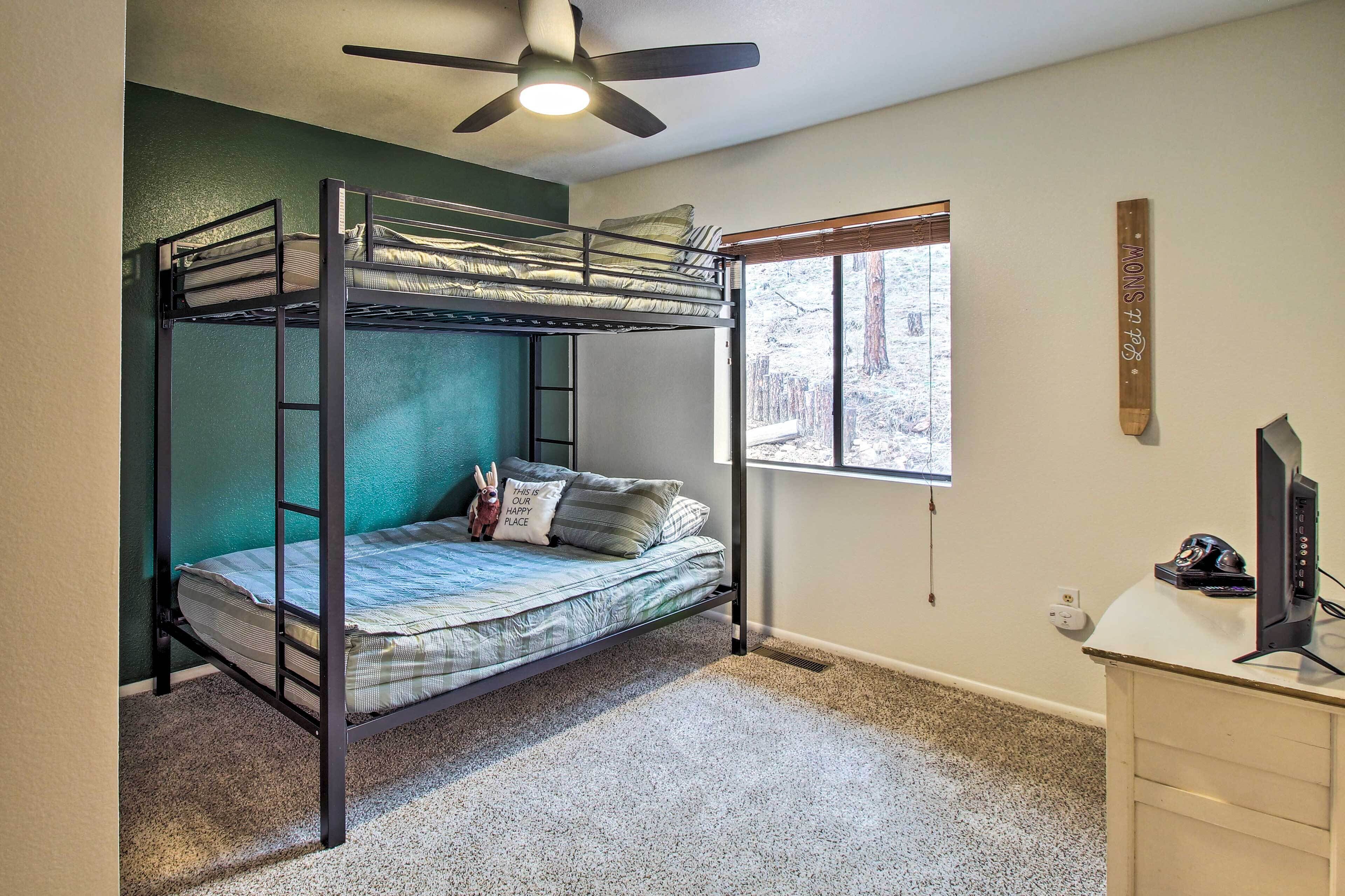 A bunk bed room with a ceiling fan, a window with a view of trees, and a desk with a computer.