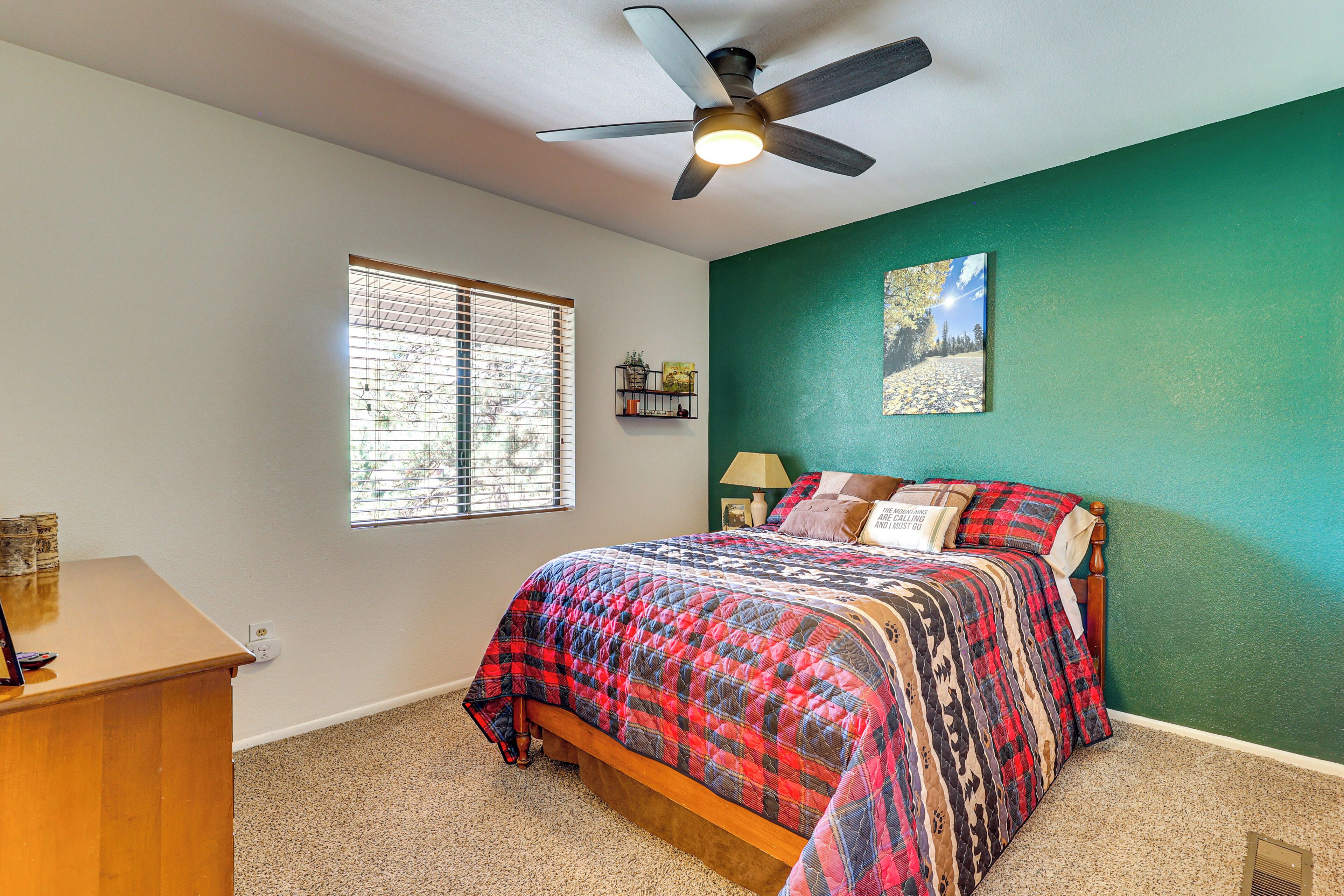 A bedroom with a bed, a ceiling fan, a window with blinds, and a green wall.