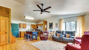 A spacious living area with a sofa, a coffee table, and a dining table with chairs. There is a ceiling fan, wooden flooring, and a view of the outdoors through a window. - Peaceful Nutrioso Cabin Retreat w/ Mountain Views! (Eagar)