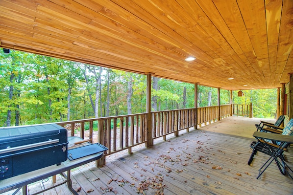 A covered outdoor deck with a grill, seating, and a view of a forest. - 300-acre Mountain Retreat in the Arkansas Ozarks (Ozark)