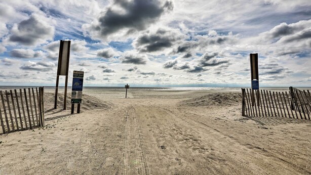 Ein Strand mit einer Holzlattenzaun und einem Wegweiser in der Mitte.