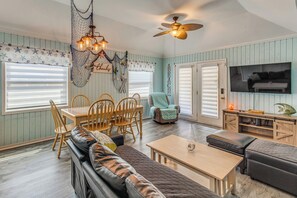 A room with a dining table, chairs, a sofa, a television, and a ceiling fan.