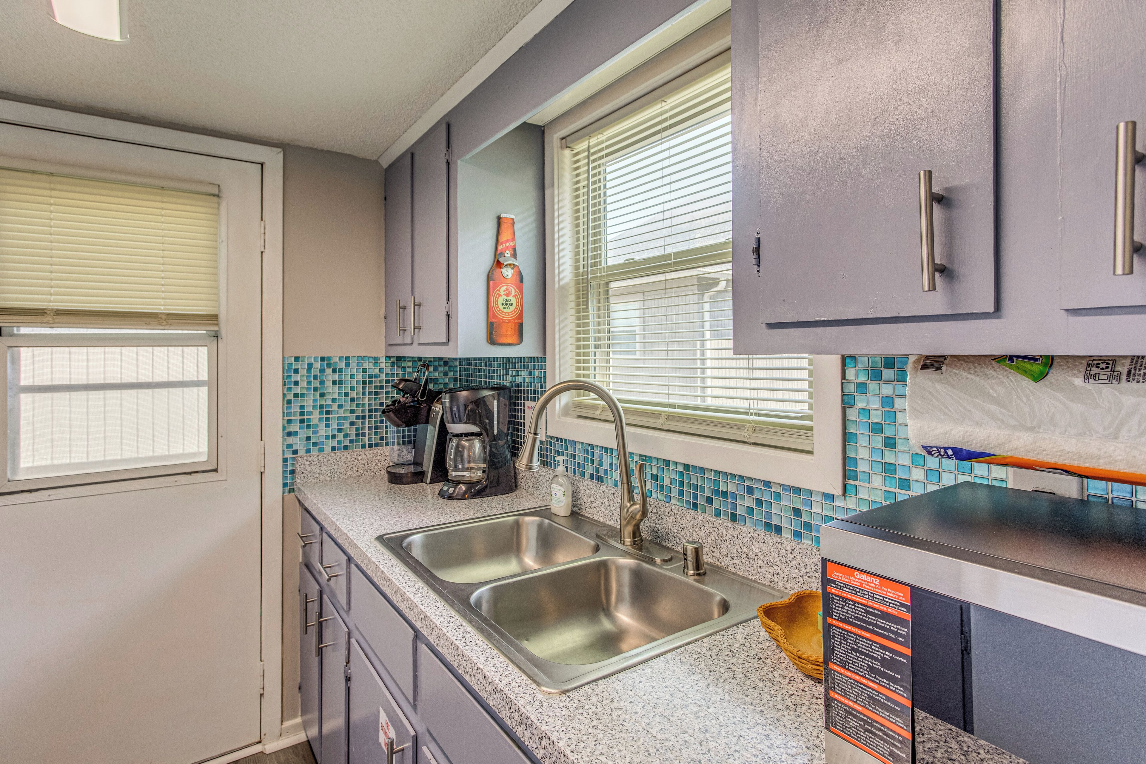 A compact kitchen with a sink, a coffee maker, and a bottle of Red Horse beer on the wall.