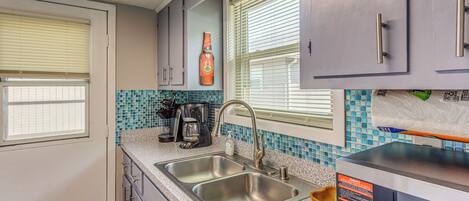 Una cocina compacta con un lavamanos, una cafetera y una botella de cerveza Red Horse en la pared.