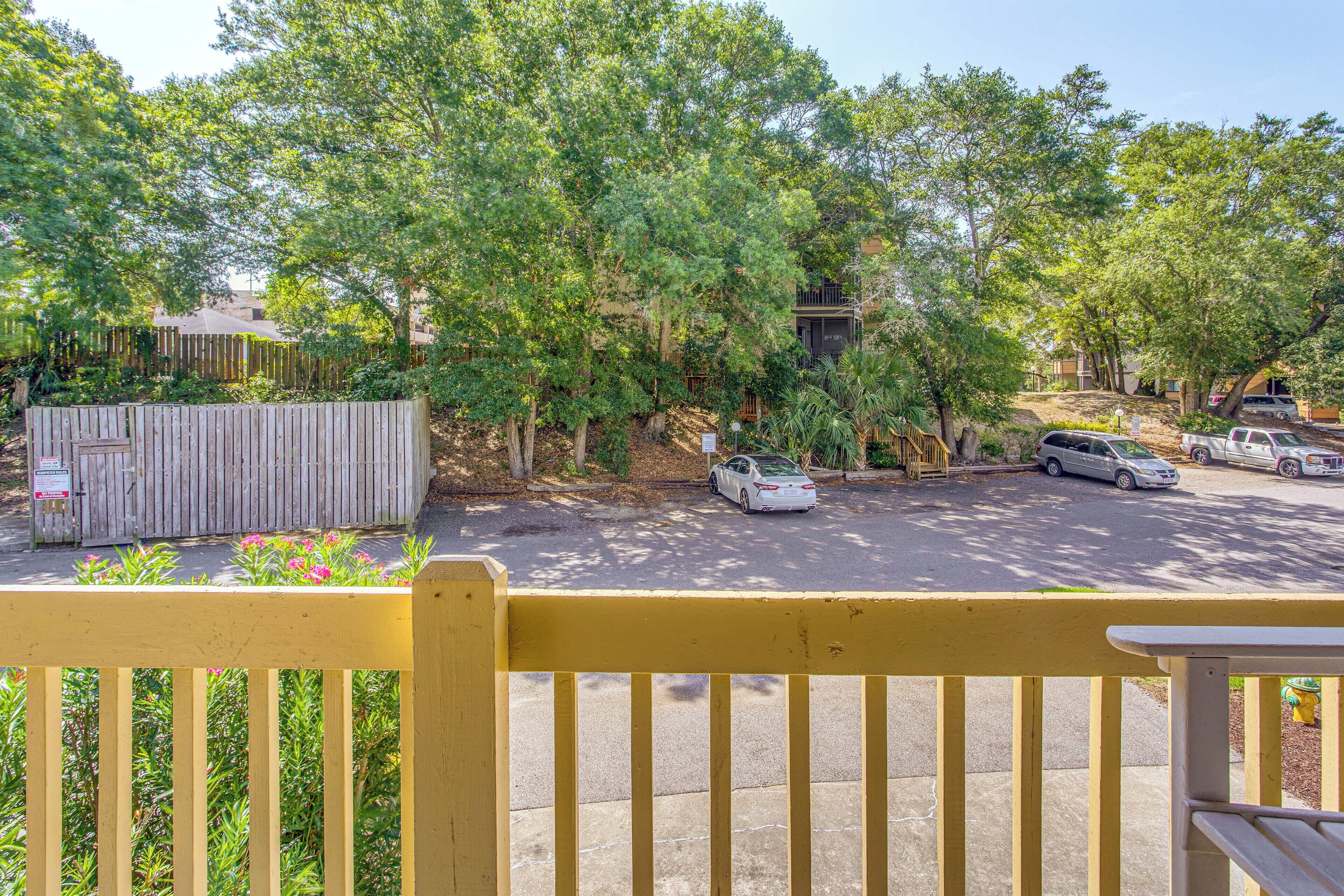 A parking area with cars, a wooden fence, and trees.