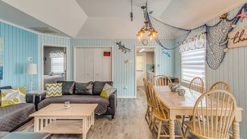 A room with a dining area, a sofa, a coffee table, and a wall with nautical decorations.