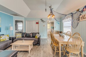 A room with a dining area, a sofa, a coffee table, and a wall with nautical decorations.