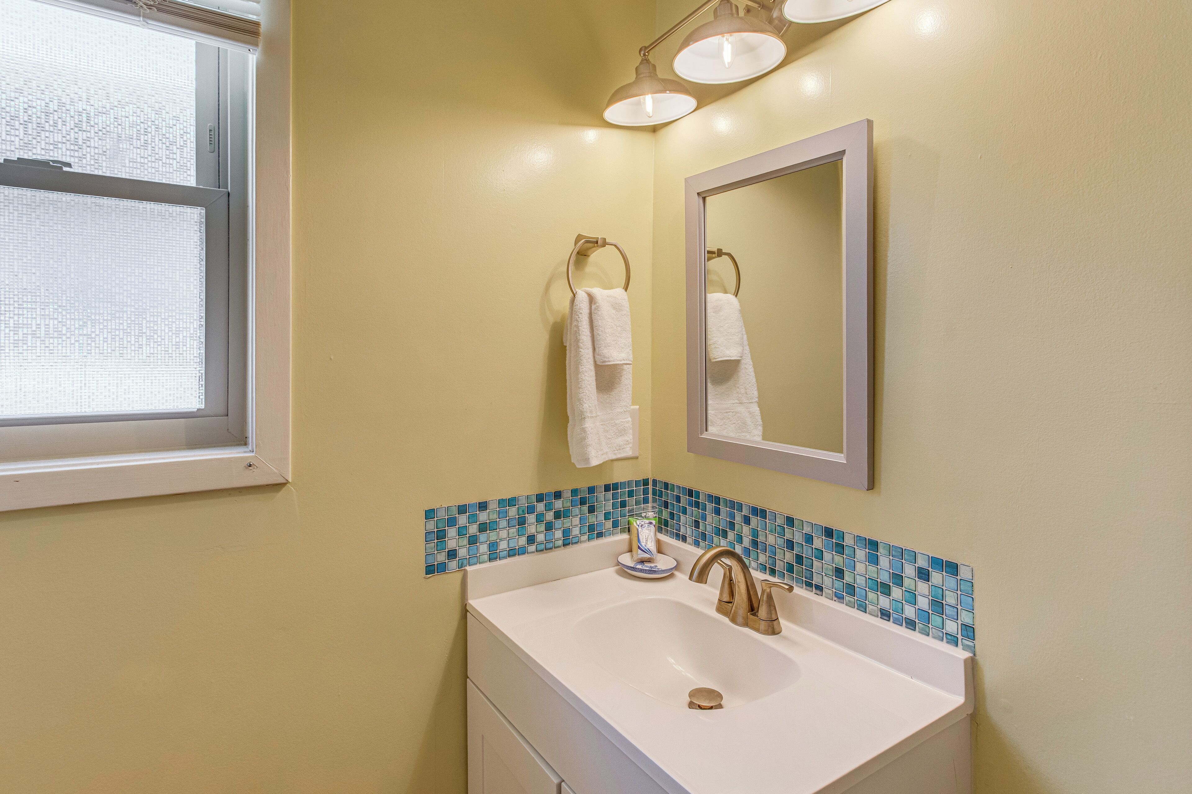 A bathroom with a white sink, a mirror, and a window.