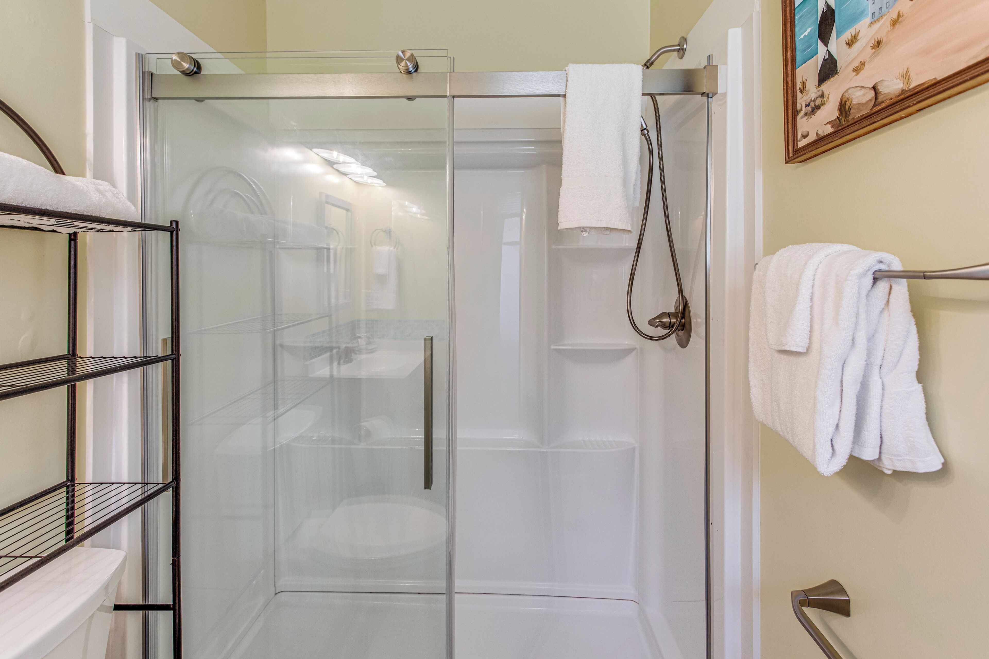 A glass-enclosed shower stall with a towel rack and a metal shelf unit beside it.